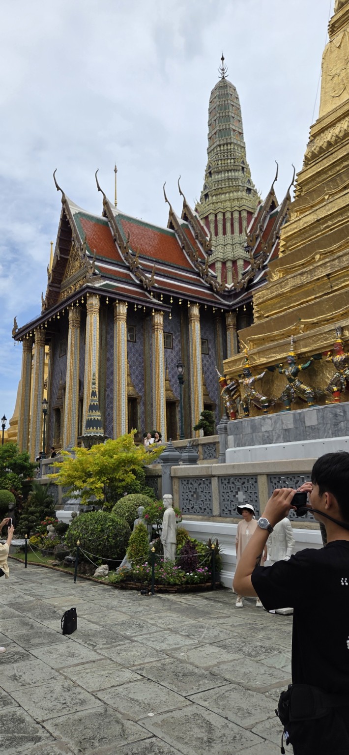 Ornate palace roofs and a tall spire beneath a cloudy Bangkok sky