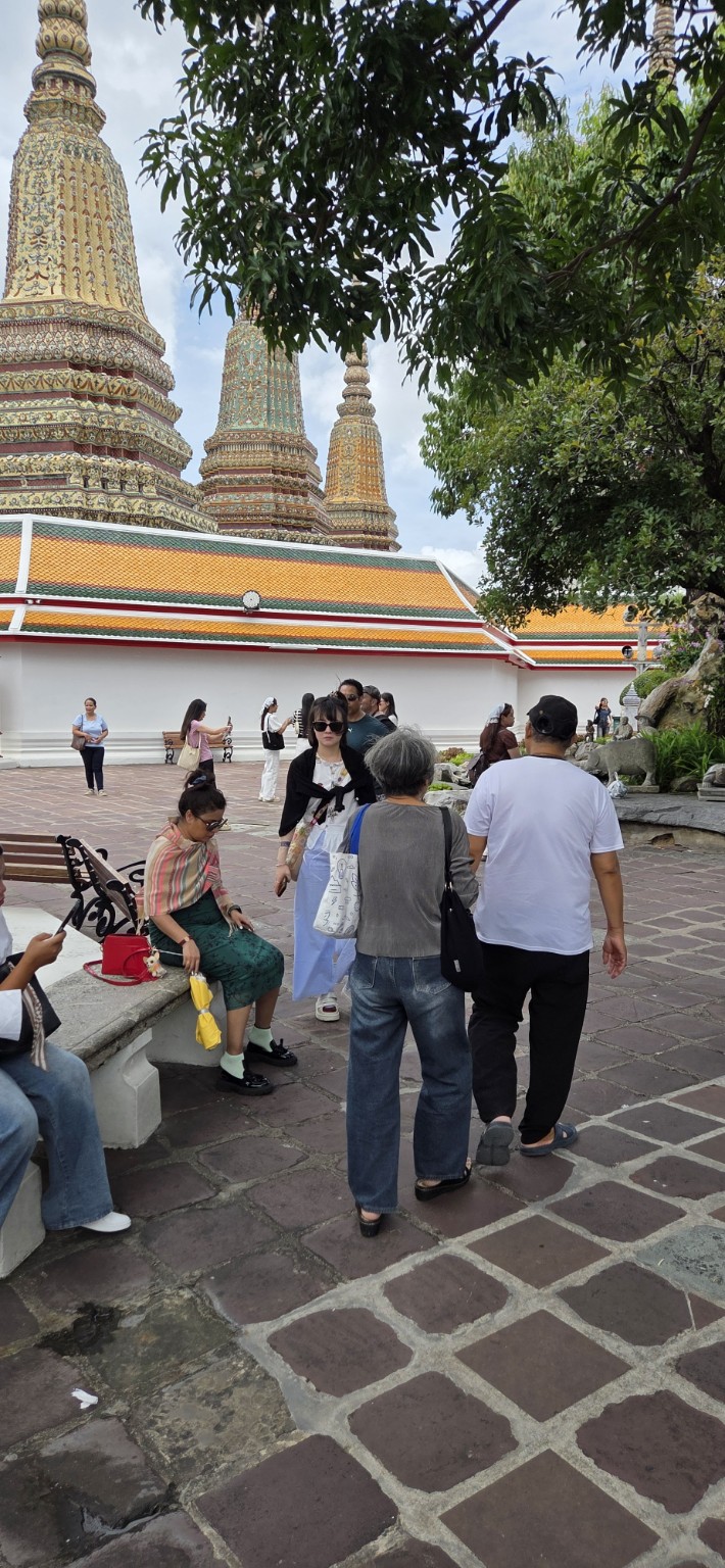 Visitors walking among colorful chedis in a shaded Wat Pho courtyard