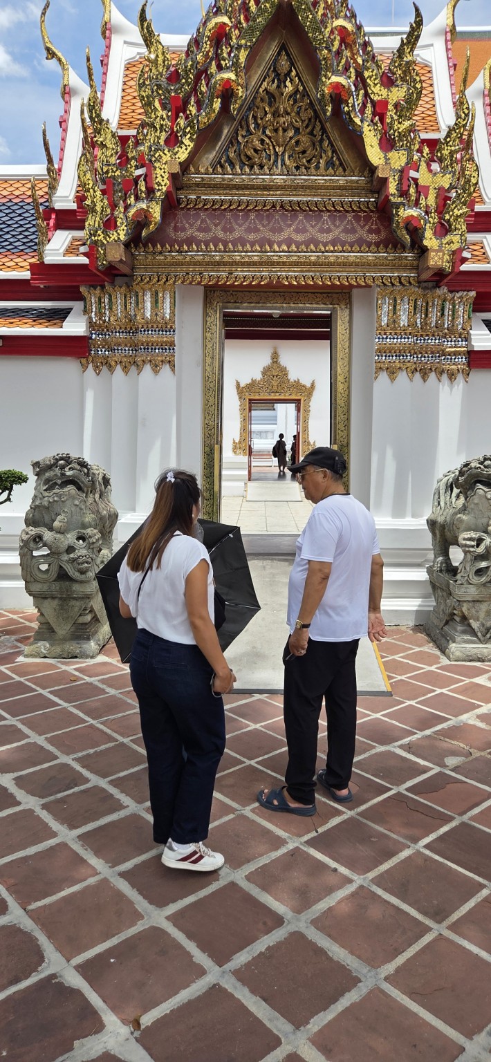Tana and her father standing between stone lions at an ornate temple doorway